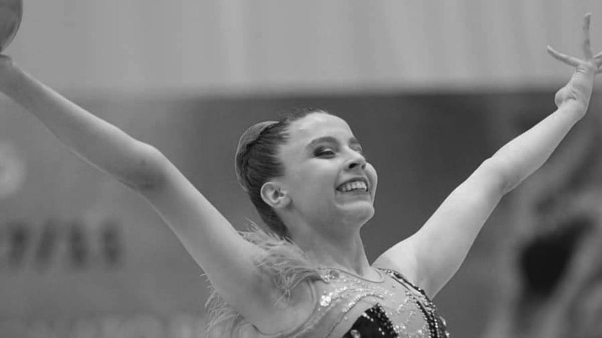 Młoda gimnastyczka artystyczna w błyszczącym stroju, z uniesionymi ramionami i uśmiechem na twarzy, podczas występu. Pod spodem widnieje napis "ISABELLE MARCINIAK 17/07/2007 - 24/12/2025".