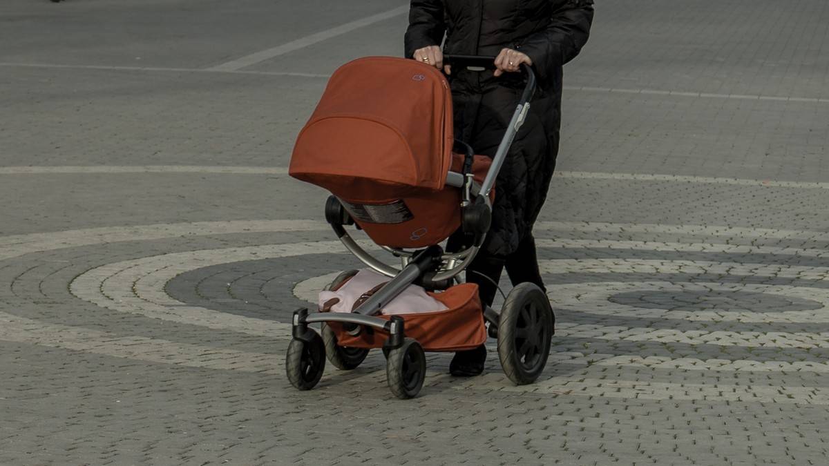 Osoba prowadząca wózek dziecięcy na zewnątrz.