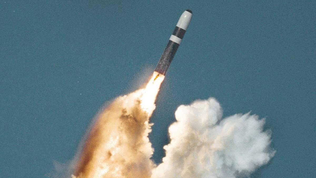 Pocisk balistyczny wystrzeliwany z wyrzutni, unoszący się na tle błękitnego nieba i kłęb&oacute;w dymu.