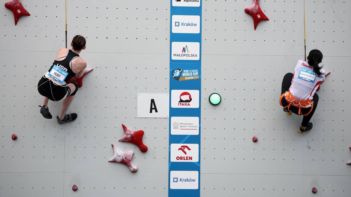 Dwóch zawodników wspina się po ścianie podczas zawodów wspinaczki sportowej. Po lewej mężczyzna w czarnym stroju, po prawej kobieta w białej koszulce i pomarańczowych spodenkach.