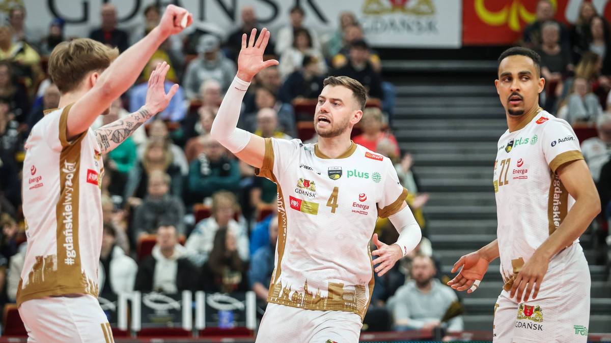 Trzech siatkarzy w białych koszulkach z brązowymi elementami na tle publiczności.