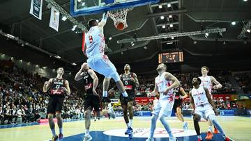 Zawodnicy koszyk&oacute;wki podczas meczu, jeden z nich wykonuje wsadu do kosza.