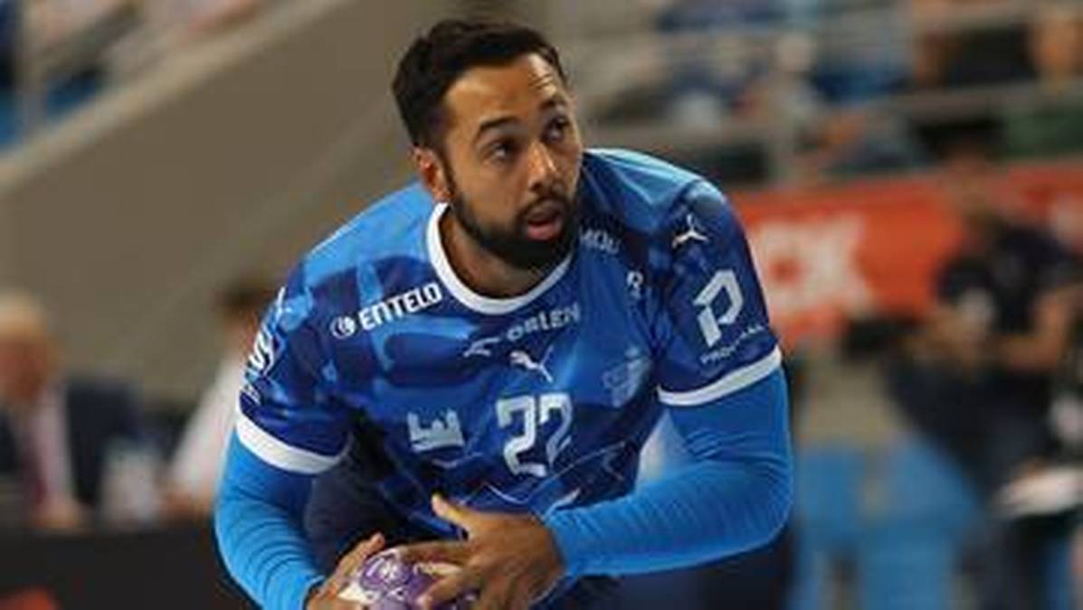 Piłkarz ręczny w niebieskiej koszulce z numerem 22, trzyma piłkę w dłoniach podczas meczu.