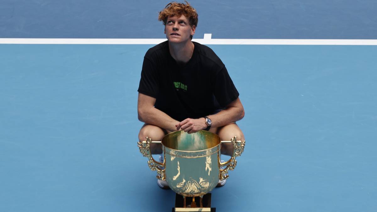 Jannik Sinner, zwycięzca turnieju tenisowego, siedzi na korcie z pucharem na kolanach.
