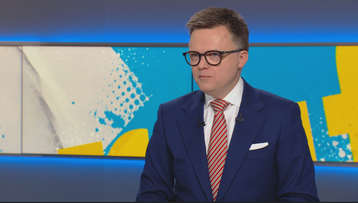 Mężczyzna w garniturze i okularach siedzi, patrząc w bok.