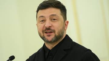 Wołodymyr Zełenski, prezydent Ukrainy, przemawia do mikrofonu w czarnym garniturze.