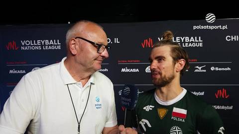 Dwaj mężczyźni stoją obok siebie przed ścianką z logo Volleyball Nations League. Starszy mężczyzna w okularach i białej koszulce rozmawia z młodszym mężczyzną w zielonej koszulce z polską flagą. Obaj patrzą w stronę kamery.