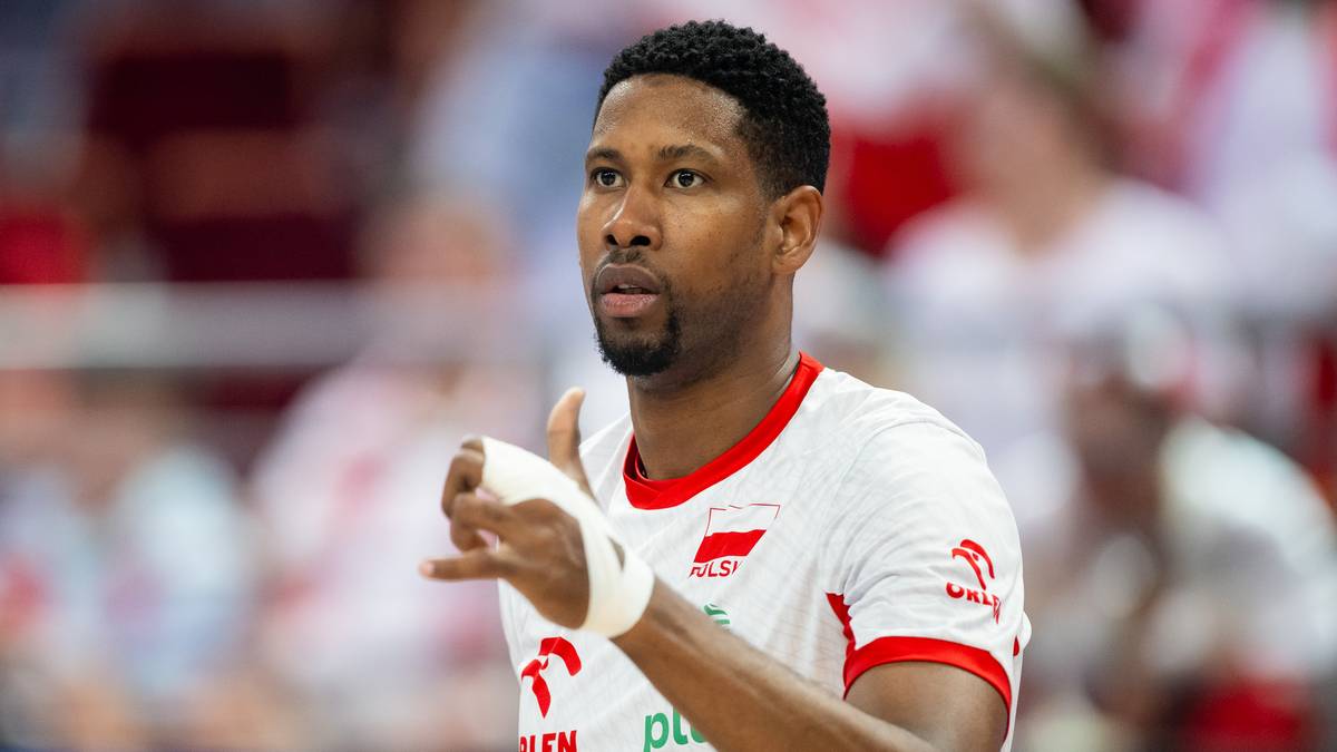 Siatkarz w białej koszulce z czerwonymi elementami i numerem 10 na rękawie, z bandażem na dłoni.