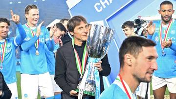 Trener Antonio Conte trzyma Puchar Superpucharu Włoch, otoczony przez radośnie świętujących zawodnik&oacute;w Napoli.