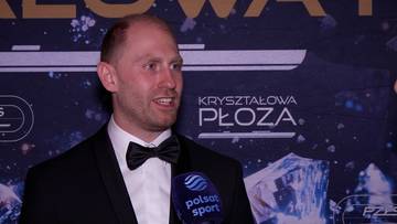 Mężczyzna w czarnym garniturze i muszce, uśmiecha się, trzymając mikrofon Polsat Sport.