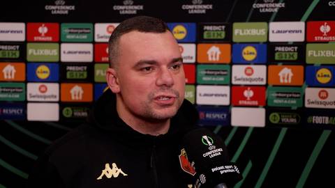 Adrian Siemieniec, trener, stoi przed ścianą z logo Ligi Konferencji Europy.