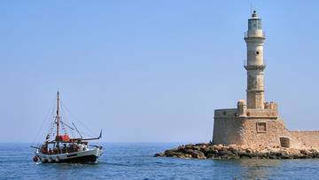 Żaglowiec płynie po morzu w pobliżu kamiennej latarni morskiej na wyspie.