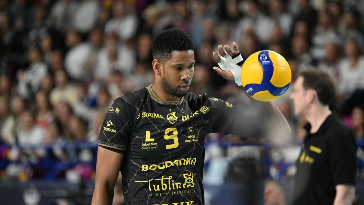 Siatkarz trzymający piłkę siatkową w prawej dłoni.