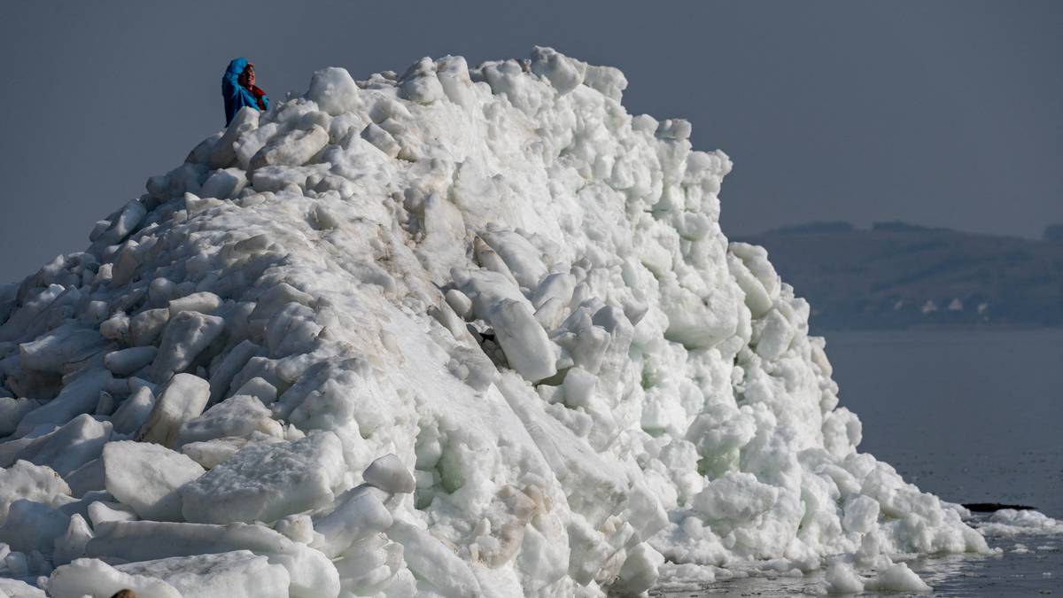 Kilka os&oacute;b stoi na szczycie wysokiej g&oacute;ry utworzonej ze spiętrzonej kry lodowej na wybrzeżu.