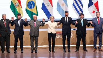 Grupa os&oacute;b pozuje do zdjęcia na tle flag Unii Europejskiej i kraj&oacute;w Mercosur.