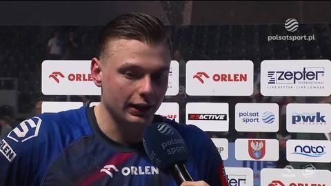 Portret mężczyzny w stroju sportowym, m&oacute;wiącego do mikrofonu.