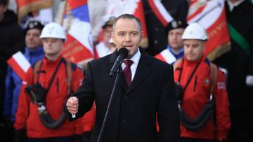 Karol Nawrocki przemawia do mikrofonu na tle grupy os&oacute;b z polskimi flagami.