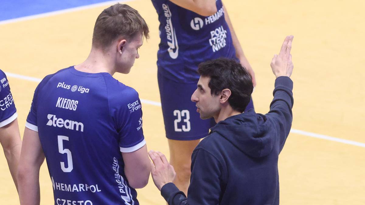 Dwóch mężczyzn w strojach sportowych rozmawia podczas meczu siatkówki, jeden z nich udziela wskazówek.