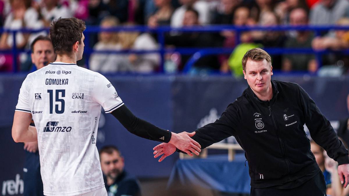 Dw&oacute;ch mężczyzn w strojach sportowych wita się na boisku siatkarskim.