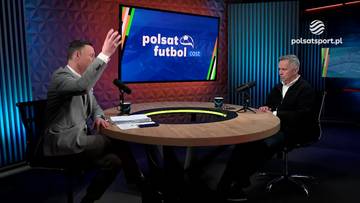 Dwóch mężczyzn siedzi przy okrągłym stole w studiu telewizyjnym. Na ekranie za nimi widnieje logo Polsat Futbol. Jeden z mężczyzn, ubrany w szary garnitur, gestykuluje prawą ręką.