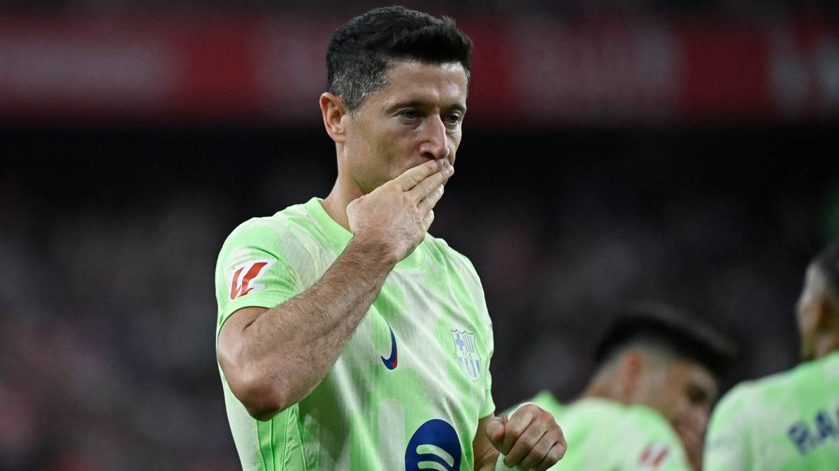 Piłkarz Robert Lewandowski w jasnej, jasnozielonej koszulce z krótkim rękawem, dotykający palcami ust i nosa.