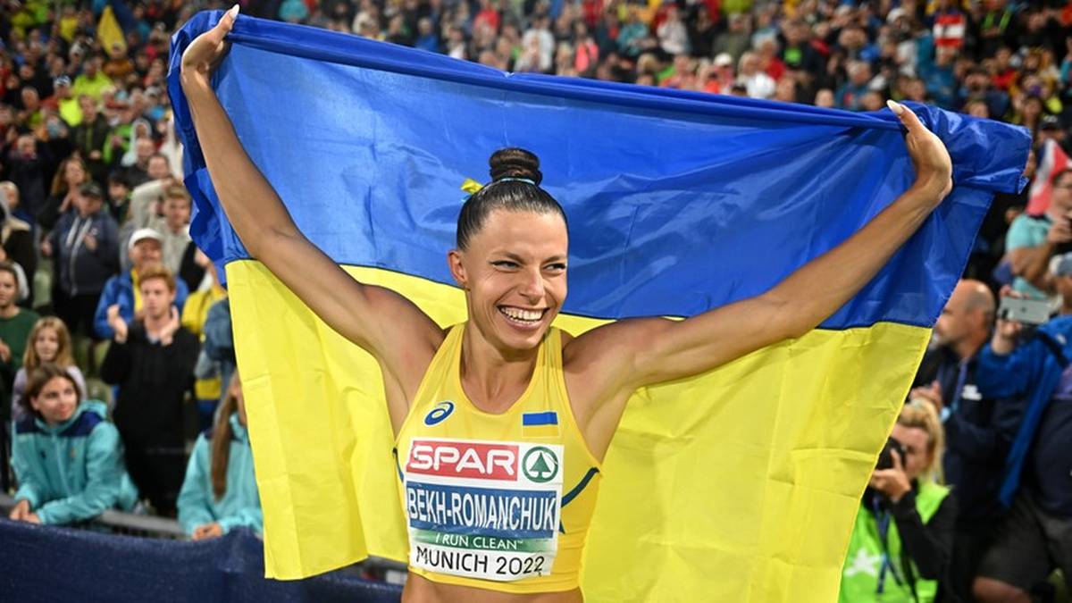 Uśmiechnięta lekkoatletka trzyma ukraińską flagę nad głową podczas zawodów.