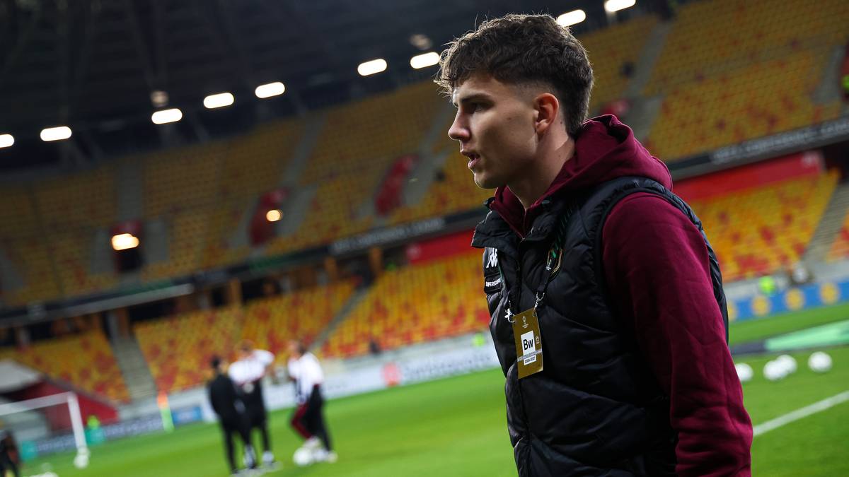 Młody piłkarz w kamizelce treningowej na tle stadionu.