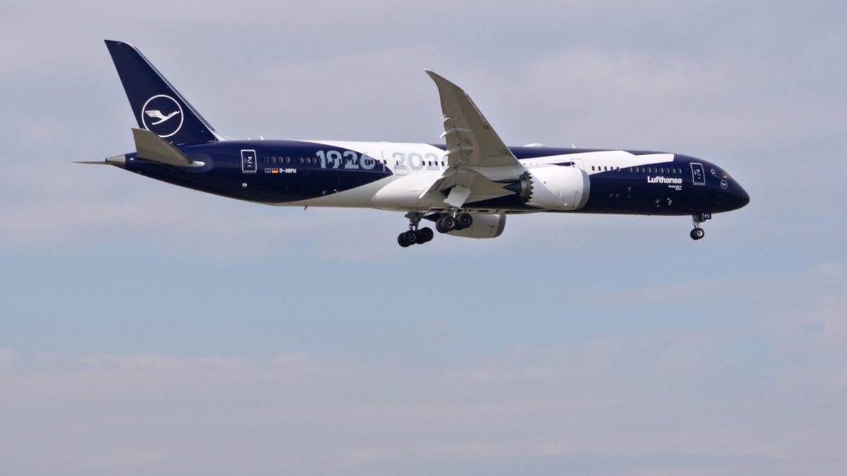 Granatowo-biały samolot pasażerski linii Lufthansa z wysuniętym podwoziem leci na tle jasnego nieba.