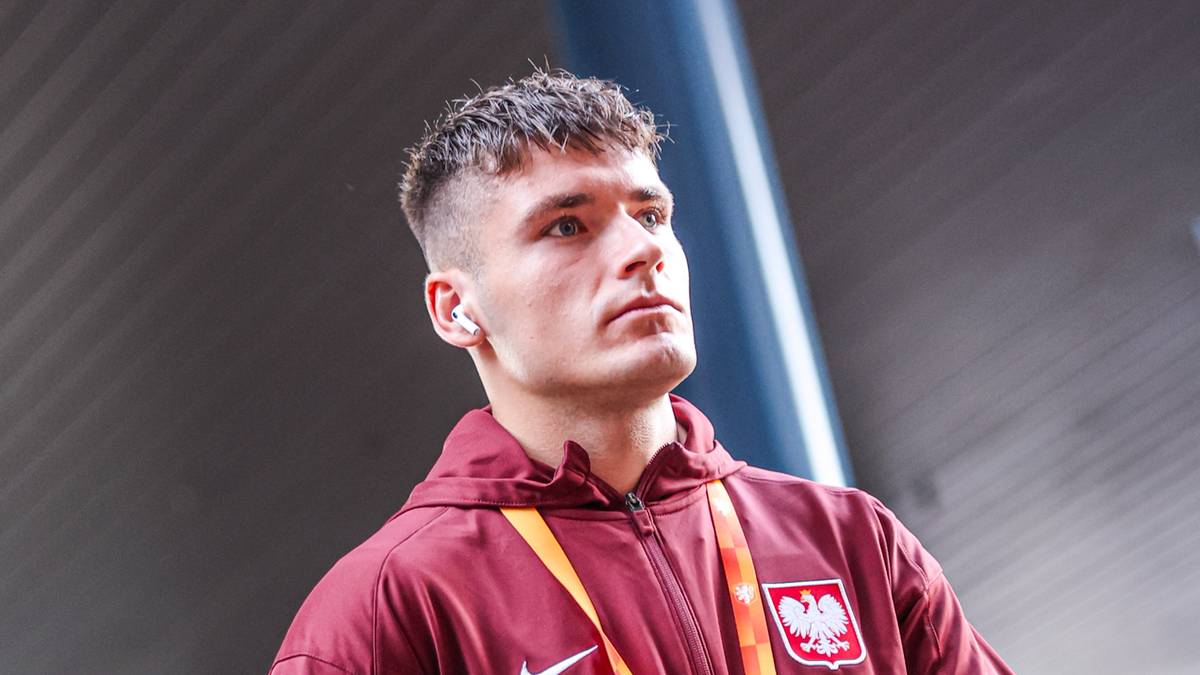 Młody mężczyzna w dresie reprezentacji Polski, z wpiętym godłem, patrzący przed siebie.