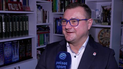 Portret mężczyzny w okularach, m&oacute;wiącego do mikrofonu z logo Polsat Sport.