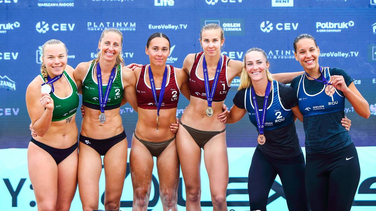 Sześć uśmiechniętych siatkarek plażowych w strojach sportowych stoi na podium, pozując do zdjęcia z medalami na szyjach.