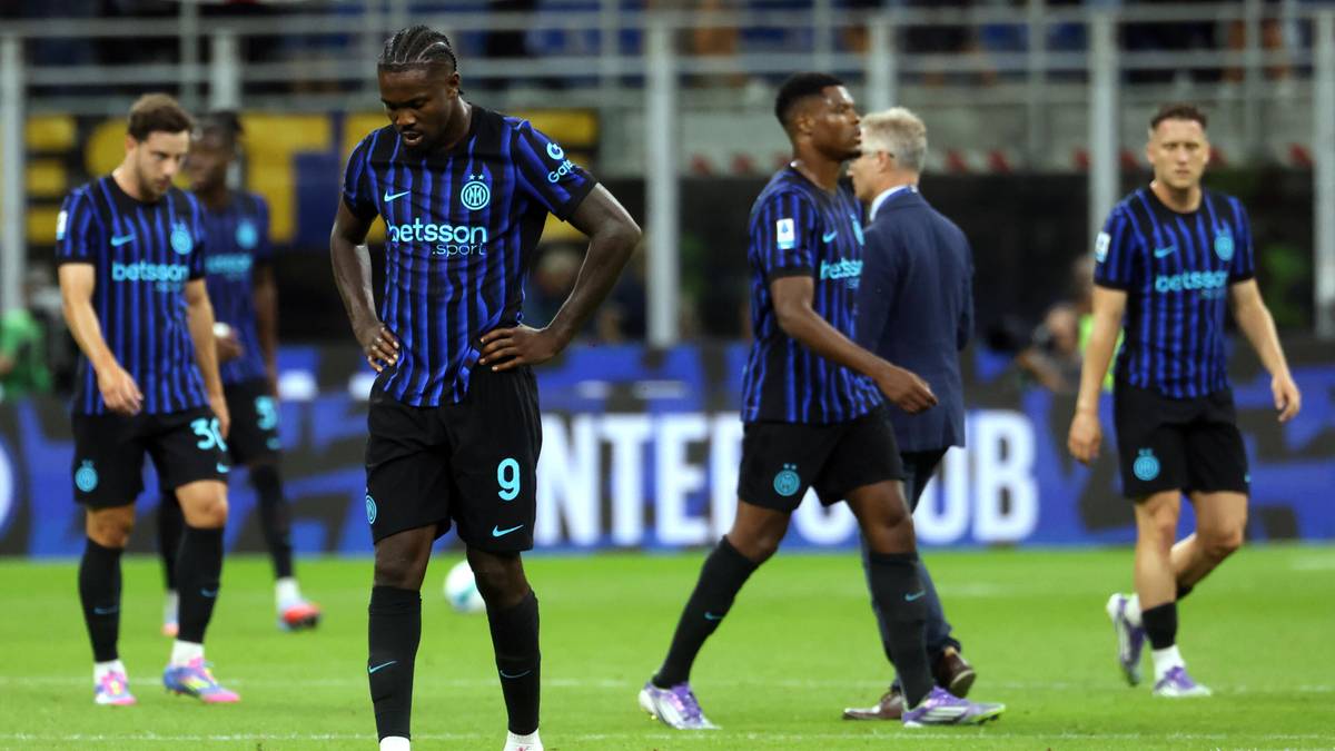 Piłkarze w niebiesko-czarnych strojach na boisku piłkarskim, niektórzy patrzą w dół.