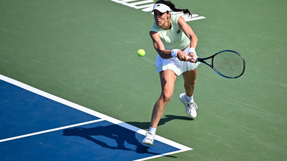 Tenisistka w białej spódniczce i jasnej koszulce z rakietą w ręku, uderzająca piłkę podczas meczu.