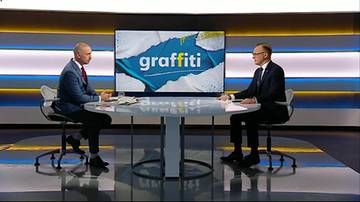 Dw&oacute;ch mężczyzn w garniturach siedzi przy okrągłym stole w studio telewizyjnym. Za nimi na dużym ekranie widnieje napis "graffiti" na tle stylizowanej grafiki.