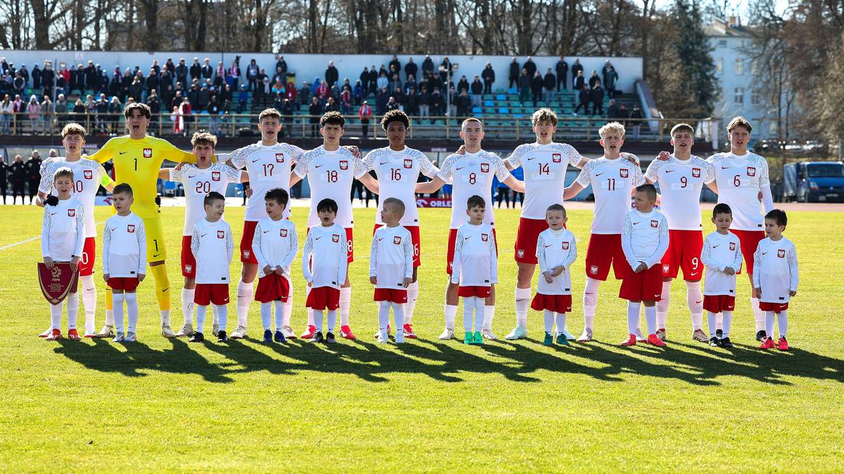 Drużyna piłkarska młodzieżowej reprezentacji Polski ustawiona w rzędzie na boisku.