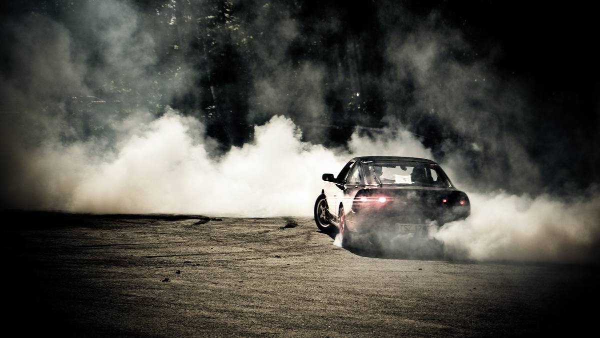 Samoch&oacute;d wykonujący drift, otoczony gęstym dymem z palonych opon w ciemności.