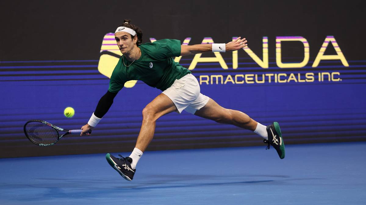 Tenisista Lorenzo Musetti w zielonej koszulce i białych spodenkach, wykonujący bekhend na korcie tenisowym.