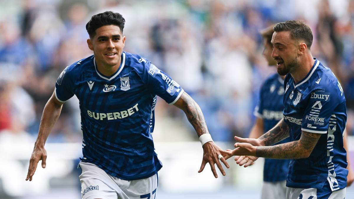 Dw&oacute;ch piłkarzy Lecha Poznań w niebieskich koszulkach z białymi napisami cieszy się z gola podczas meczu.