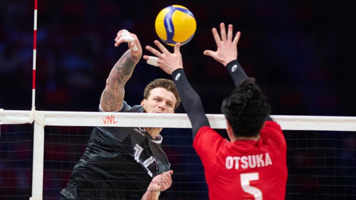 Dwóch siatkarzy w akcji podczas meczu. Jeden zawodnik w czarnym stroju blokuje atak drugiego zawodnika w czerwonym stroju.