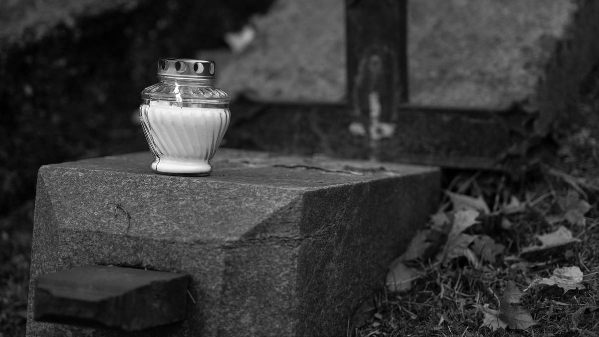 Szklany znicz na kamiennym postumencie nagrobka na cmentarzu.