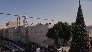 Plac w Betlejem udekorowany na Boże Narodzenie, z widocznym dużym drzewkiem świątecznym i tłumem ludzi zgromadzonych przed bazyliką.