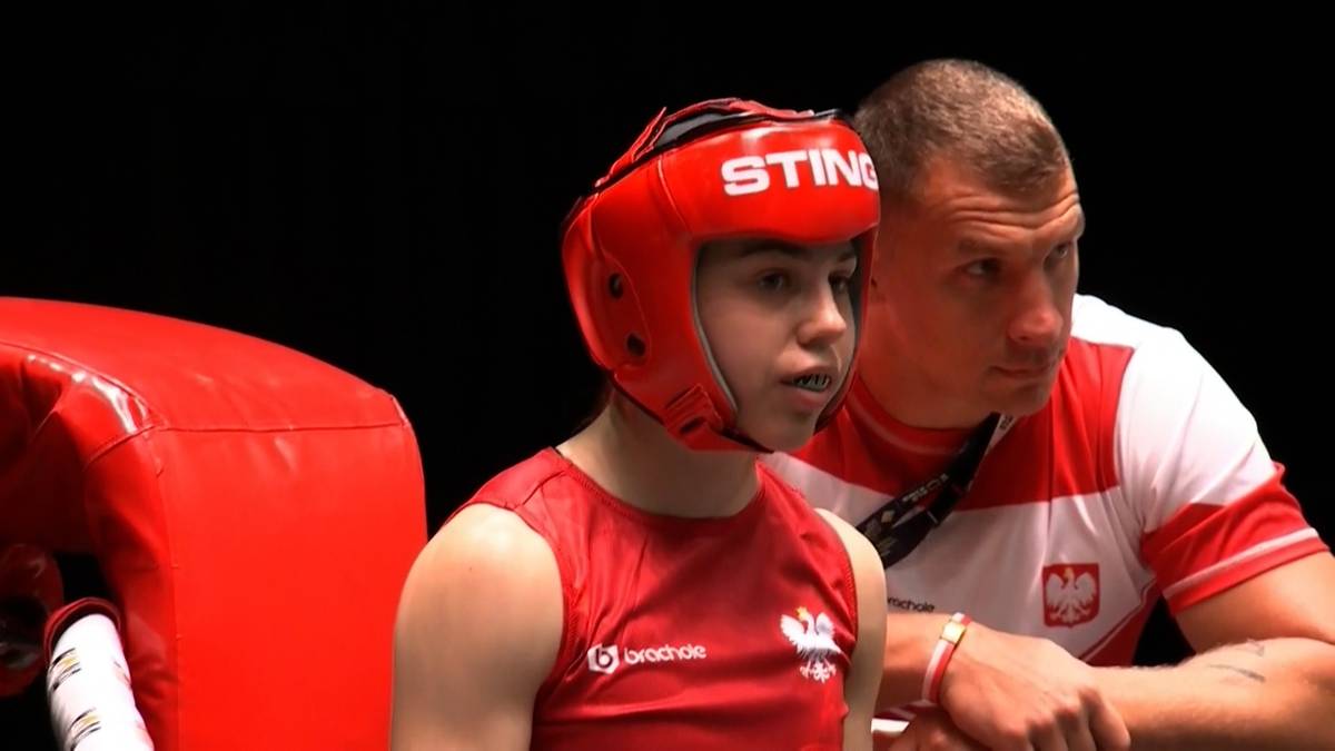 Młoda bokserka w czerwonym kasku i koszulce z herbem Polski, obok niej stoi trener.