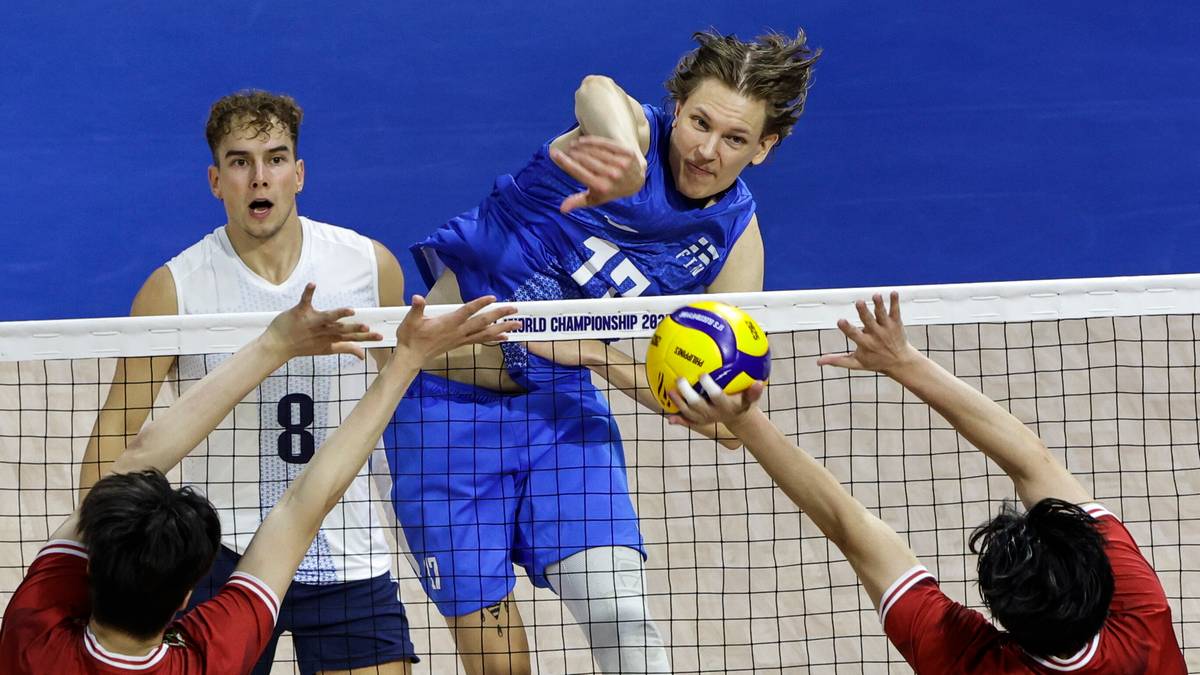 Siatkarz w niebieskim stroju wykonuje atak, celując piłką w pole przeciwnika. Pozostali gracze na siatce próbują ją zablokować.