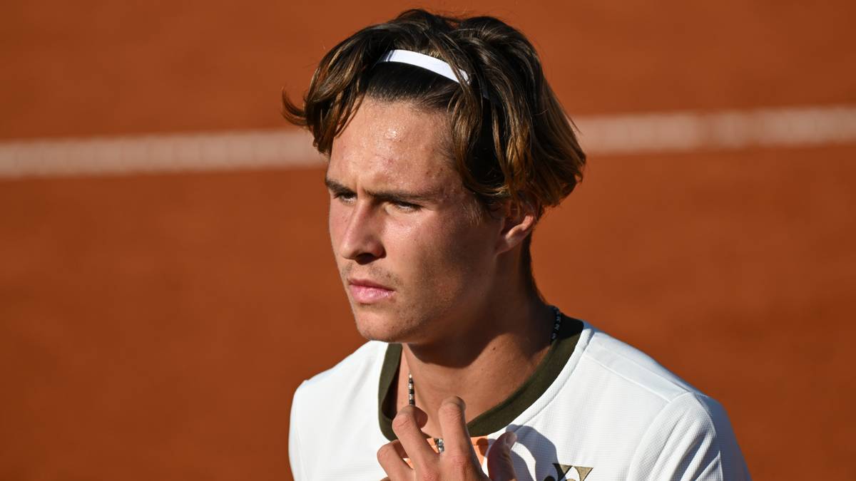 Młody tenisista na korcie ziemnym, skupiony na grze.