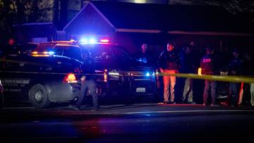 Policja zabezpiecza miejsce strzelaniny, na którym widać radiowozy z włączonymi sygnałami świetlnymi i taśmę policyjną.