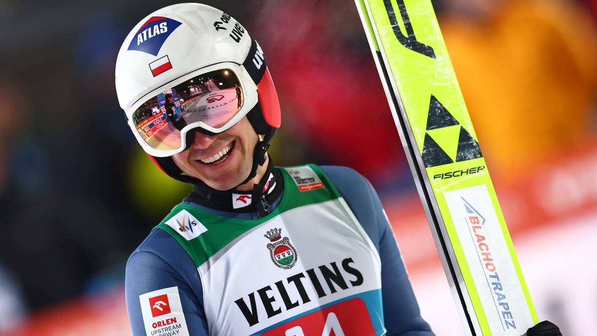 Skoczek narciarski w kasku i goglach trzymający nartę.