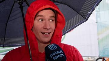 Mężczyzna w czerwonej bluzie z kapturem, trzymający parasolkę i mikrofon Polsat Sport.