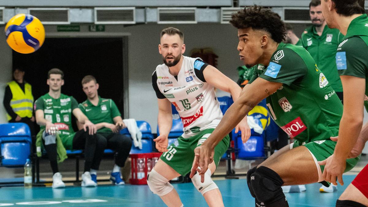 Siatkarz z numerem 15 na koszulce w pozycji obronnej, z piłką siatkową w powietrzu.