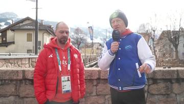 Dw&oacute;ch mężczyzn stoi na zewnątrz, jeden z nich trzyma mikrofon i m&oacute;wi do niego.