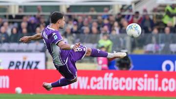 Piłkarz w fioletowym stroju kopie piłkę w powietrzu na tle trybun i reklam.